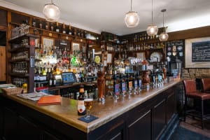 View from the corner of the bar. Hand pulls are lined up from Left to Right with a vast array of alcoholic bottles around the back.