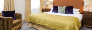 Large double bed with cabinets either side and lamps on top. With a small sofa on the left hand side.