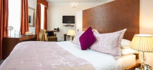 Large Double bed in fron of a desk and open plan living room.